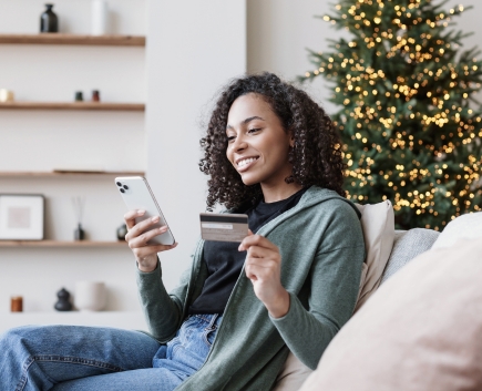 Happy woman with phone and credit card by christmas tree