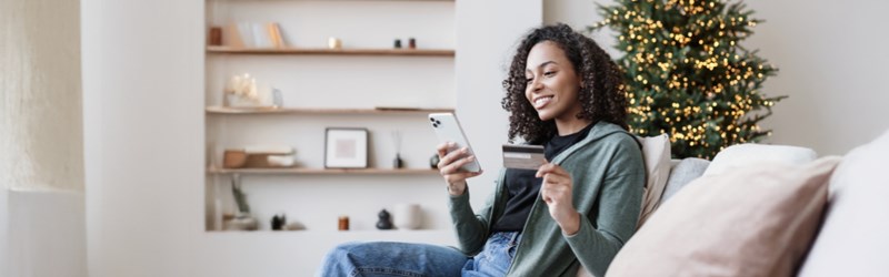 woman holding phone and credit card by christmas tree